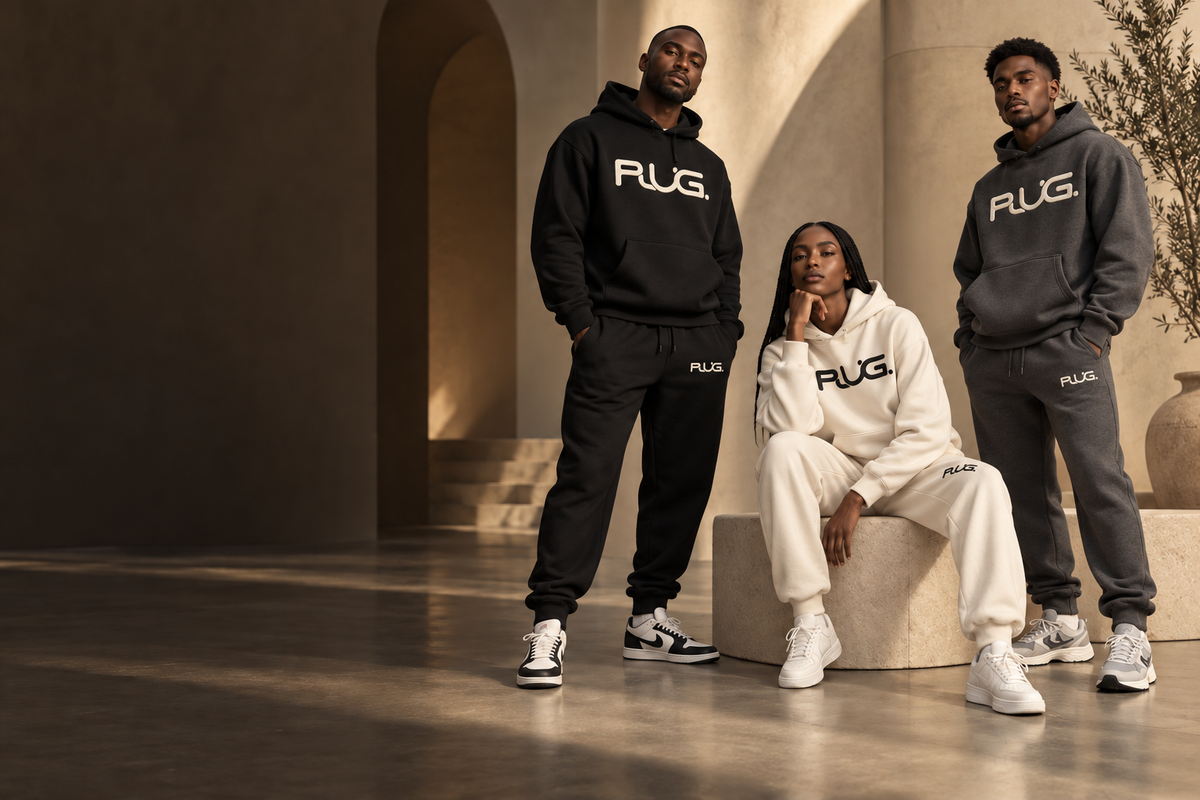 Three models wearing PLUG embroidered sweatsuits in black, cream, and dark gray in a warm stone setting.